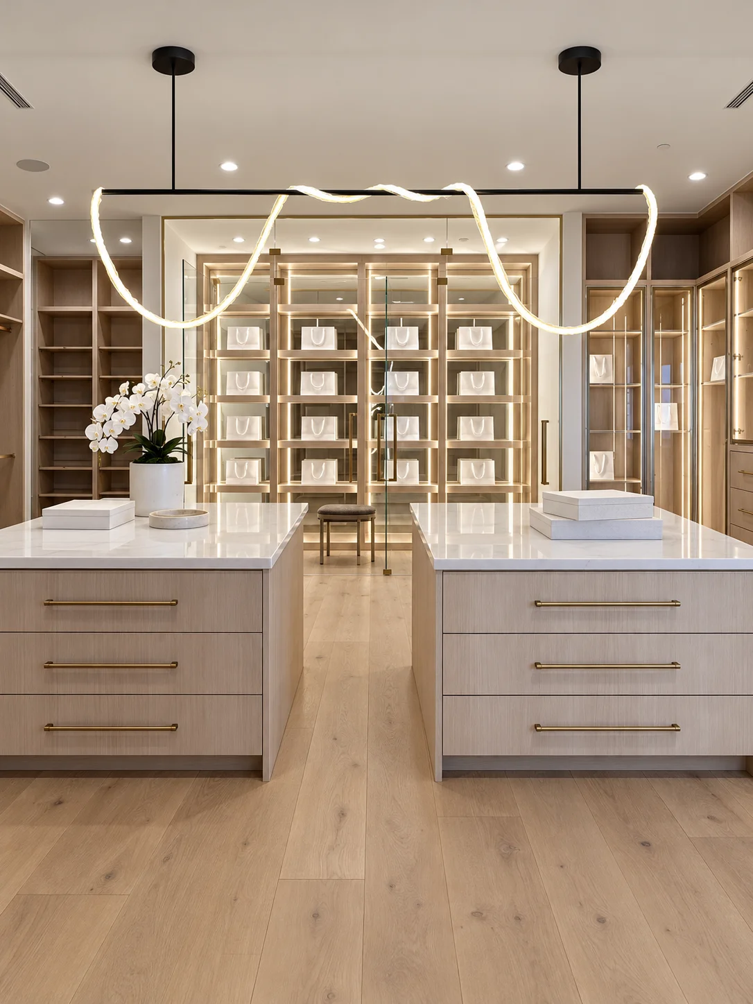 Custom oak closet with illuminated glass cabinetry, two storage islands and sculptural pendant lighting at Bridle Trail in Hidden Hills