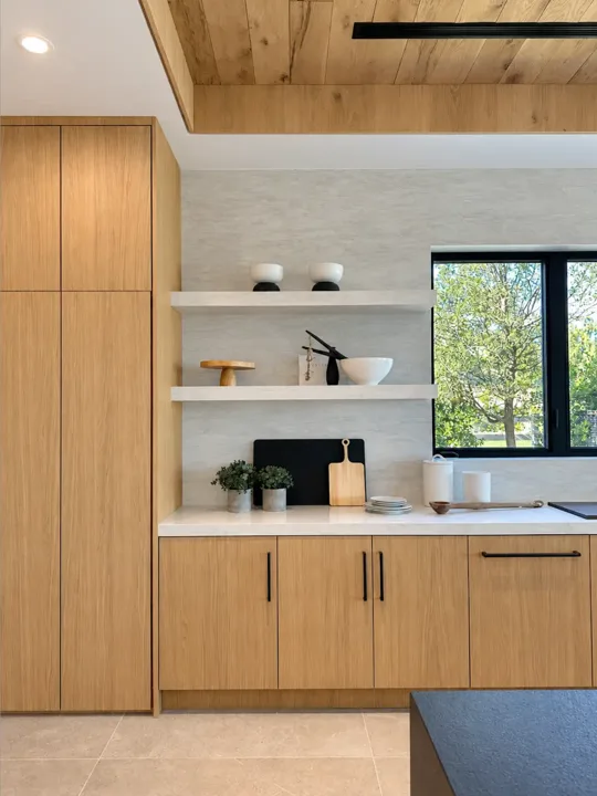 Oak kitchen cabinetry with white counters and open shelves beside a black-framed window