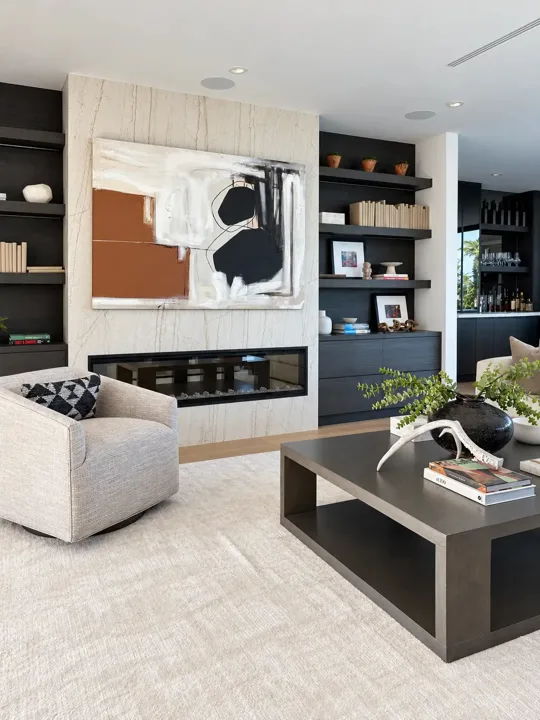 Living room with a marble fireplace, abstract artwork, dark built-in shelving and a sculptural coffee table