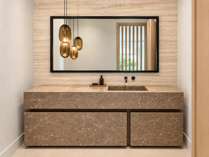Stone vanity with pendant lights and a black-framed mirror