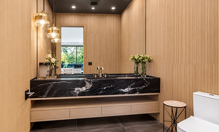 Black stone vanity with brass fixtures and wood-paneled walls