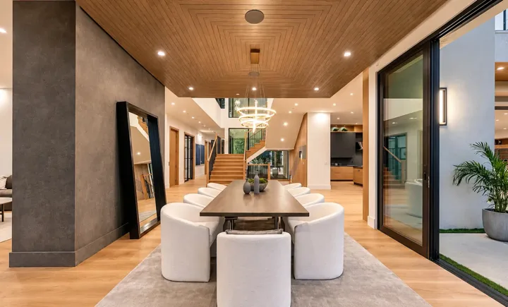 Dining room with a geometric oak ceiling, ring pendant lighting, white upholstered chairs and an open staircase