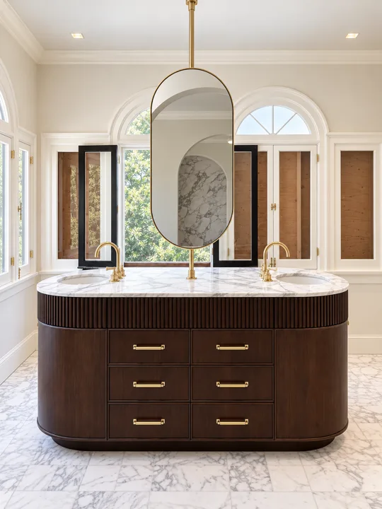 Curved fluted wood vanity beneath oval mirrors