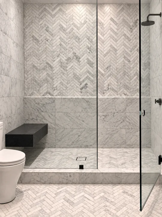 Shower with herringbone marble tile and a dark floating bench